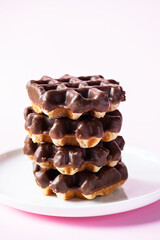 Stack of chocolate waffles served on a white plate. Close up and pink background.