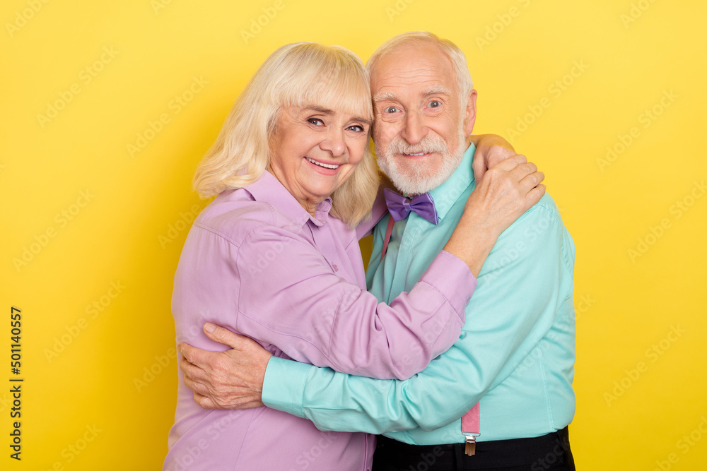 Poster portrait of two attractive cheerful grey-haired people hugging romance isolated over bright yellow c