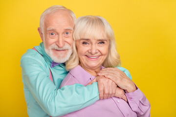 Portrait of two attractive cheerful grey-haired spouses bonding amour isolated over bright yellow...