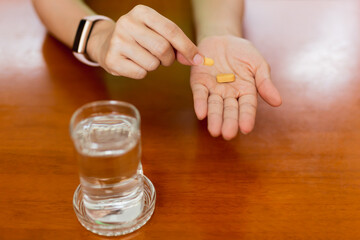 woman hands holding Vitamin C pills with glass of water on table.