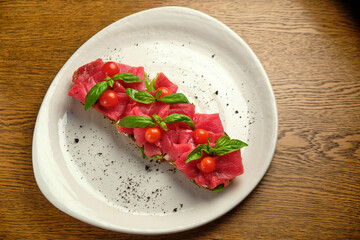 Bruschetta with red pickled meat on a white plate