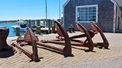 Old rusted anchors in display in front of an old wooden building in Edgartown port