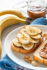 Toast with tasty nut butter and banana slices on light background. Walnut, hazelnut and cashew nut spread in glass jar. Homemade breakfast sandwich. Healthy food concept. Selective focus.