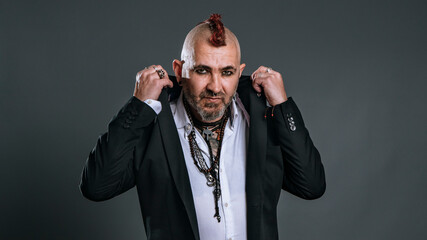 elegantly dressed punk man lifts lapels of his jacket looking defiantly at camera in studio shot