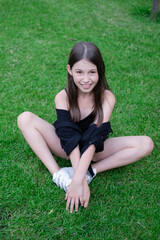 portrait of adorable teen brunette girl in black clothes outside. charming ukrainian child enjoying summer holidays vacation on green grass. pretty kids concept