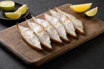Delicious smoked halibut slices served with lime on black background. Close up. Copy space.