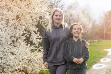 Young mother and child daughter together, hugging and joyfully laughing while relaxing in spring flowers while on a holiday. Family outdoors lifestyle.
