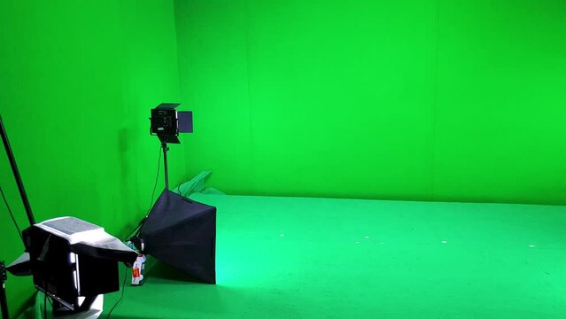 A filming studio simple setup with green screen walls and floor, lighting and softbox equipment ready for a video shoot session