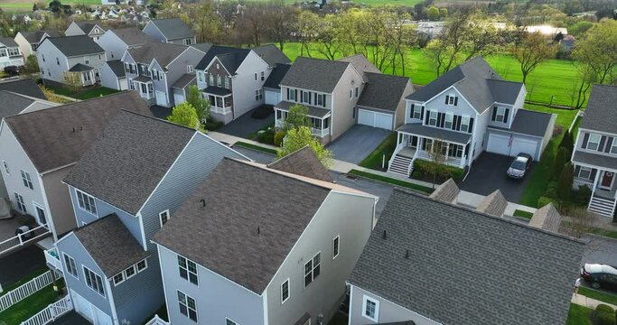 Street with new homes in spring season. Single family houses and residential construction in USA planned community. Aerial from backyard to front exterior reveal as car drives by.