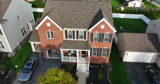 Traditional new two story modern brick family home with American flag at porch, two car garage. Aerial orbit at spring golden hour. USA pride.
