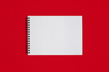 Notebook made of white paper with binding on a red background. Empty notepad without notes with...