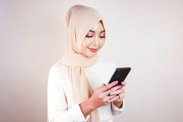 Portrait of cheerful young Muslim Asian woman smiling while looking at her cellphone