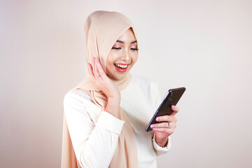 Fototapeta premium Portrait of cheerful young Muslim Asian woman smiling while looking at her cellphone