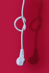 Electric plug for a socket with a knot on a cable on a red background. The concept of the inability...
