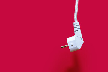 Electric plug for a socket on a red background. The concept of electricity and its importance in everyday life. Electric plug without socket. There is no way to get electricity. Free space for text