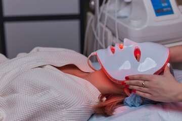 LED light anti-aging mask for facial skin care in a spa slow motion. A woman lies on a couch in a...