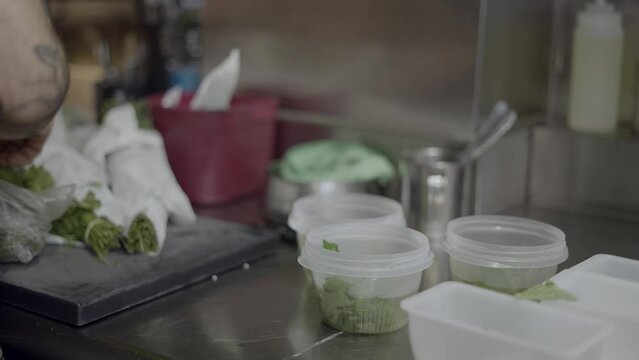 Restaurant chef sorts herbs into containers on kitchen counter, slomo