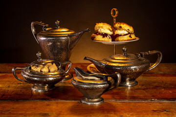 Still life with a vintage tea set and delicious scones with jam and cream, also served on vintage tableware.