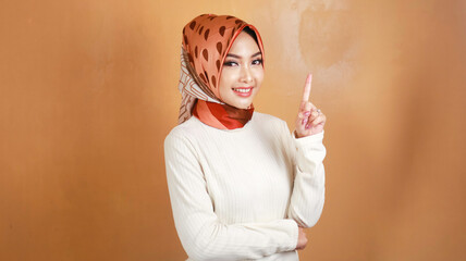 Obraz premium Cheerful young Muslim Asian woman pointing above to copy space with smile
