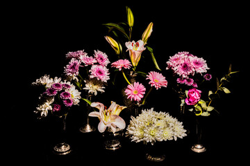 A still life of beautiful pink and white flowers, in vintage vases, against a black background.