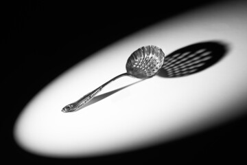 Close up of an Edwardian sifter spoon, in the spotlight, with a dramatic shadow.