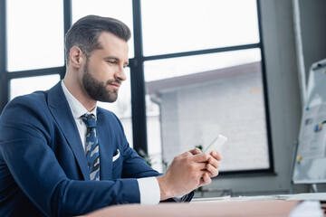 Fototapeta na wymiar businessman in blazer messaging on smartphone while sitting in office.
