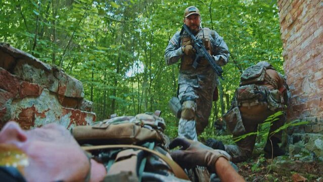 Close up military medics provide first aid to a wounded soldier wears gloves. Examine the body. In forest
