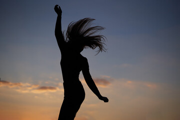 Freedom, triumph or success concept. Silhouette of attractive caucasian elegant girl dancing at sunset or woman performing modern dance outdoor in sunny day against blue cloudy sky. High quality image