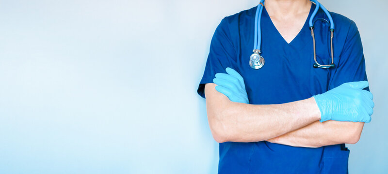 Cropped image of handsome male surgeon doctor with stethoscope in blue uniform with crossed arms in clinic on blue background. banner with copy space