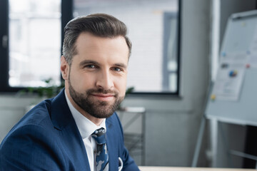 positive brunette economist looking at camera in blurred office.