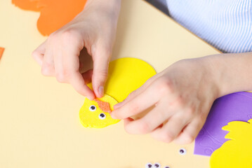 The hand of a caucasian teenage girl sticks a bird's beak sticker of orange felt with her fingers while sitting at a table