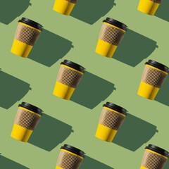 Pattern of yellow paper coffee cups on a green background. Flat lay