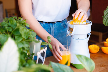 Unrecognizable woman making fresh orange juice in a kitchen full of plants.