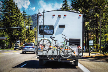 Camper with two bicycles tied to back on tree-lined highway outside of Lake Tahoe with mountains in...