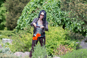 A girl with long black hair in glasses takes pictures of large red poppy flowers in the garden with her phone. Blurred background. Selective focus.