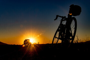 The silhouette of a bicycle with traveling box by the rural road with sunset.