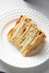 Piece of Napoleon cake with vanilla buttercream custard and crispy crusts on a white plate against a light concrete background