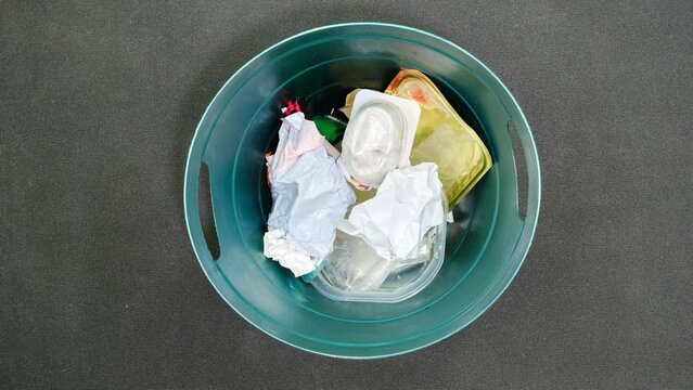 Plastic trash can being filled with household garbage and food leftovers, stop motion