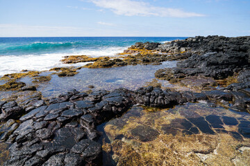 Fototapeta na wymiar Tide pools on columnar jointed volcanic lava rock in South Point Park, the southernmost point of the United States on the Big Island of Hawaii in the Pacific Ocean