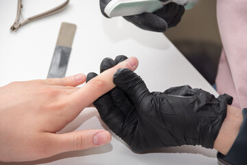 Gloved hands of a skilled manicurist filing a young woman's nails with a nail file. Hands during a...