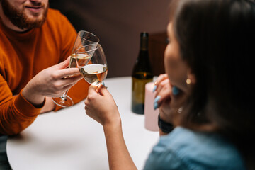 Close-up cropped shot of unrecognizable young couple clinking glasses of wine at table with candles in dark room. Loving man and woman celebrating anniversary, Valentines day, enjoying romantic date.