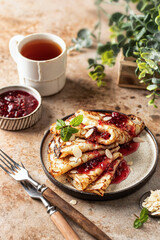 Crepes with raspberry jam and a mint leaf in brown plate. Breakfast composition