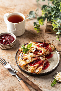 Crepes with raspberry jam and a mint leaf in brown plate. Breakfast composition