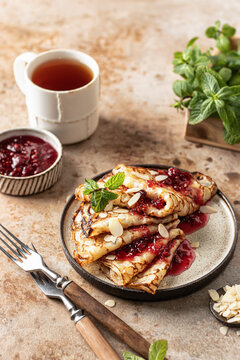 Crepes with raspberry jam, almond petals and a mint leaf in brown plate. Breakfast composition