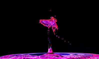 As red water was dropped into blue water, they mixed and splashed to create a shape that looks like a purple bird, or angel, hovering around a light.