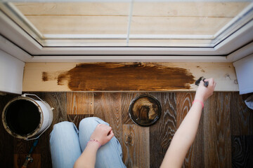 hand with a brush covers a wooden board threshold with dark impregnation (oil), top view