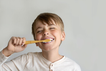 Child boy brush teeth eco wooden toothbrush, smiling, isolated on light background. Boy's dental...