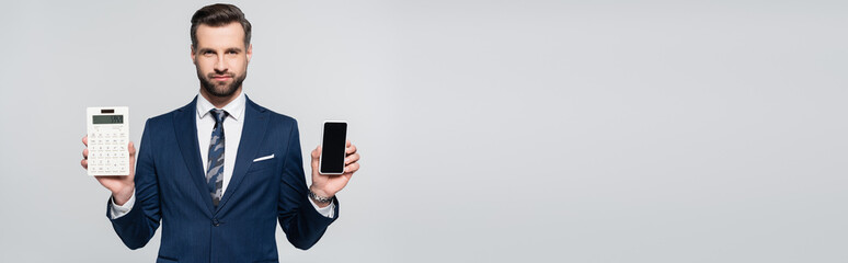businessman in blue suit holding cellphone with blank screen and calculator isolated on grey,...