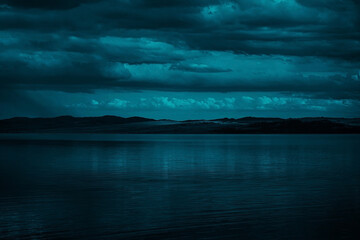 Blue-green clouds over the sea. Toned dark water and sky. Background with space for design....