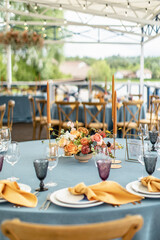 Wedding decor in blue. Banquet tables with tablecloths are decorated with compositions of flowers, on the tables are plates, glasses and candles
